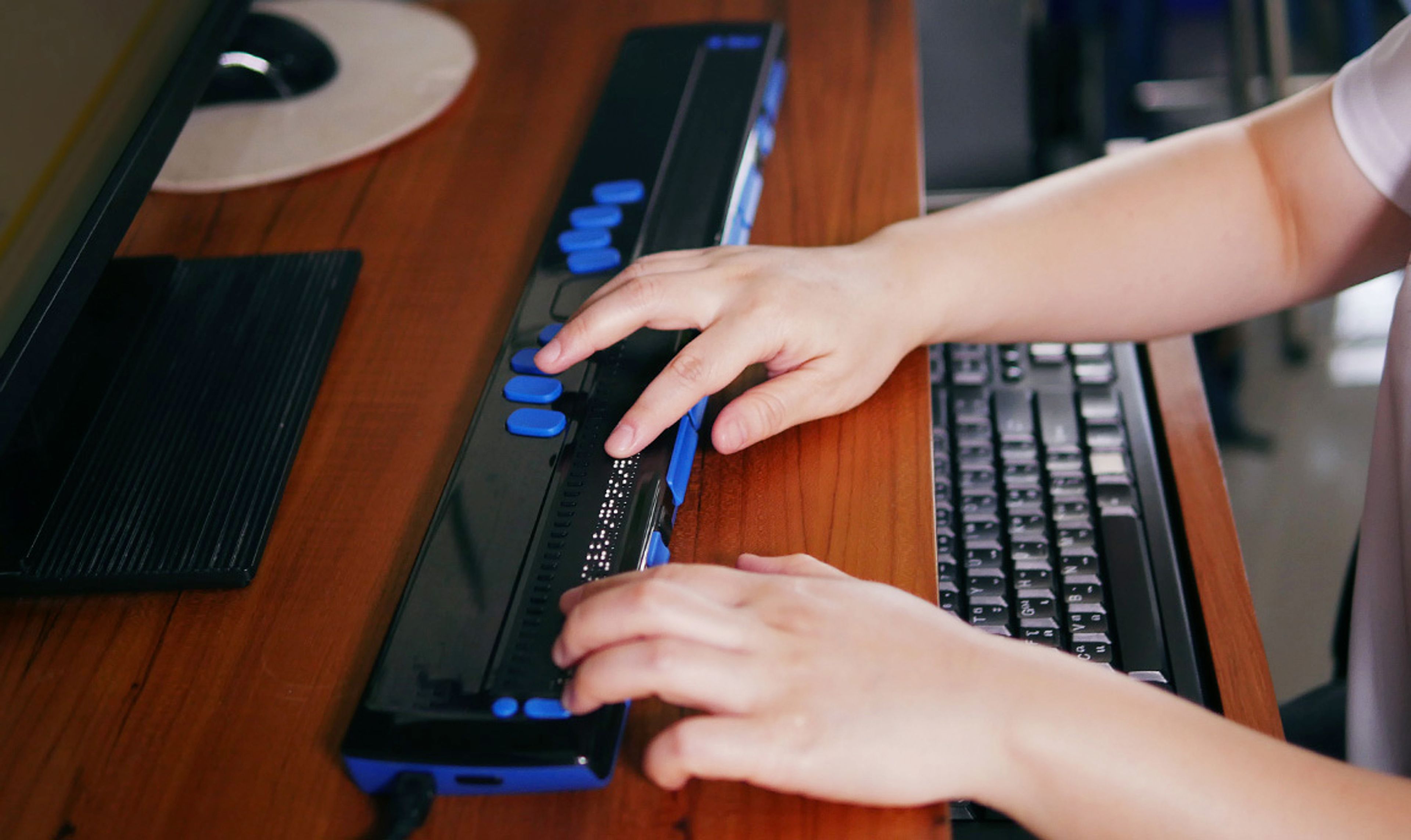 Two hands typing on a digitally accessible Braille keyboard