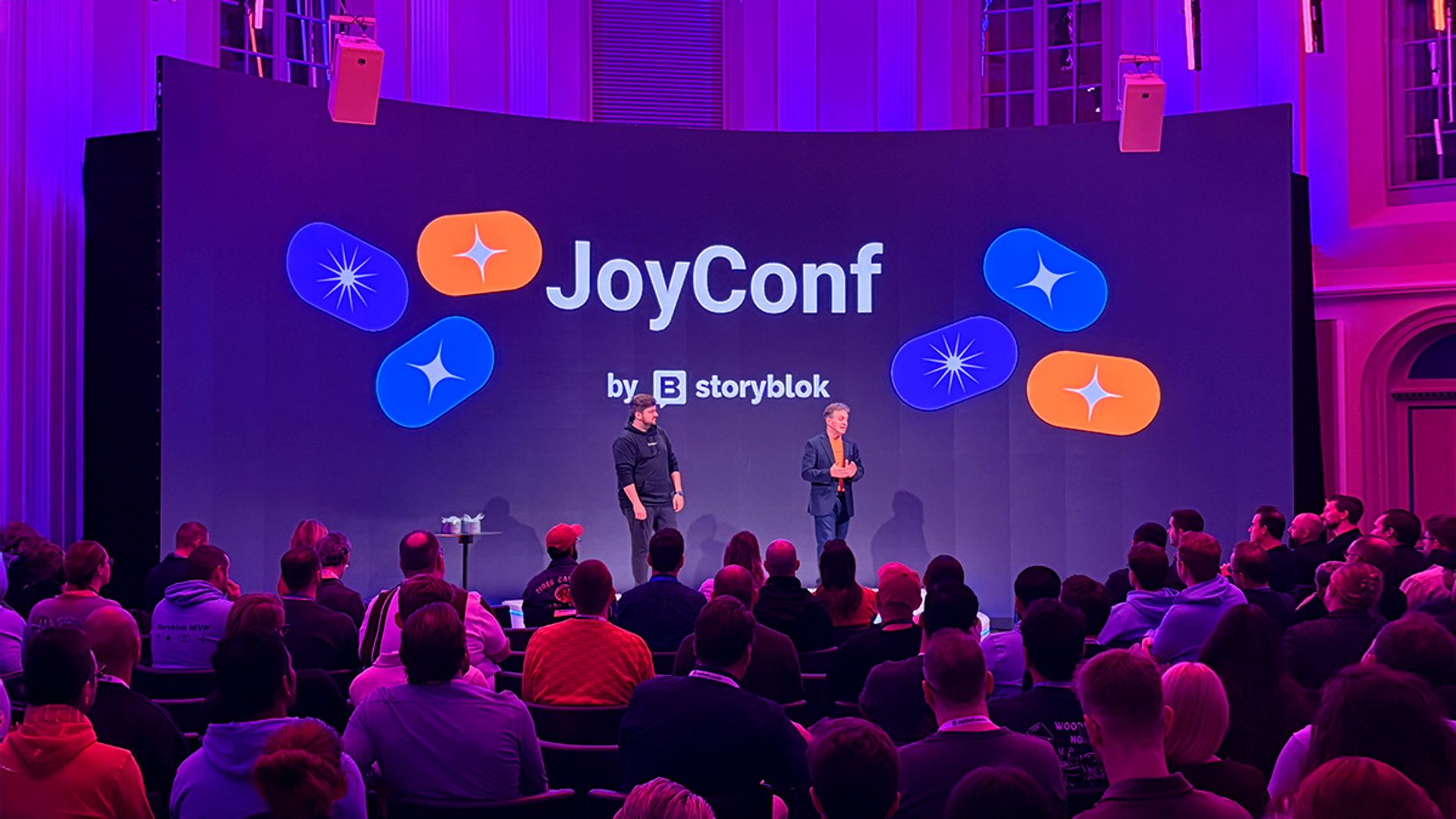 JoyConf 2025 stage with two people standing in front of a crowd.